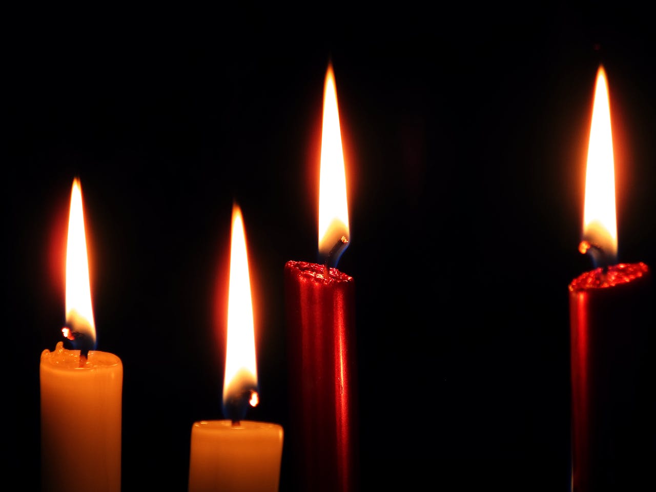 Mastering the First Impression: Your intriguing post title goes here Four colorful taper candles burning brightly against a dark background, creating a warm ambiance.